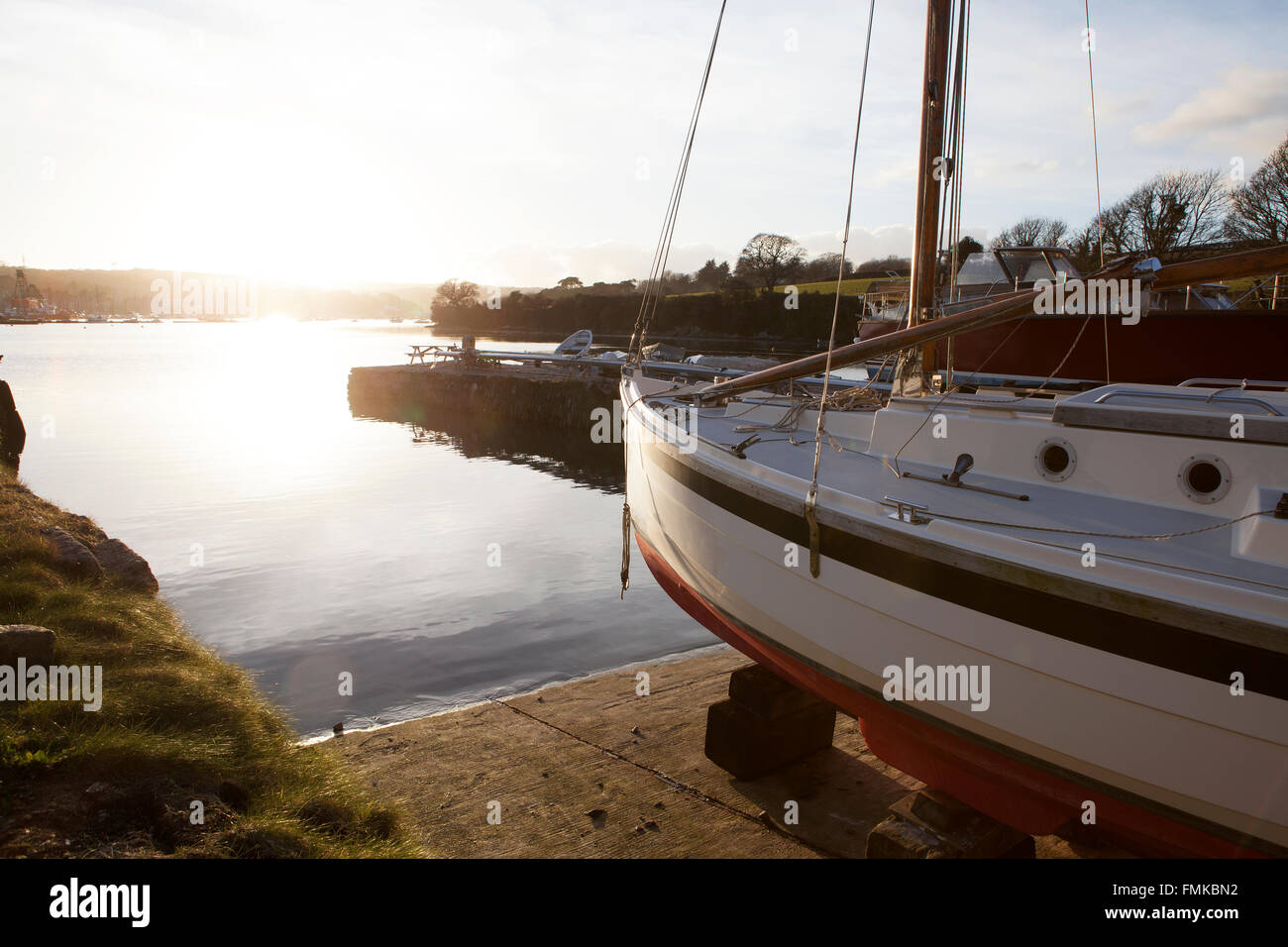 La lumière du soleil du soir brille sur la coque d'un petit yacht au bord de l'eau dans un chantier naval de Cornouailles au coucher du soleil Banque D'Images