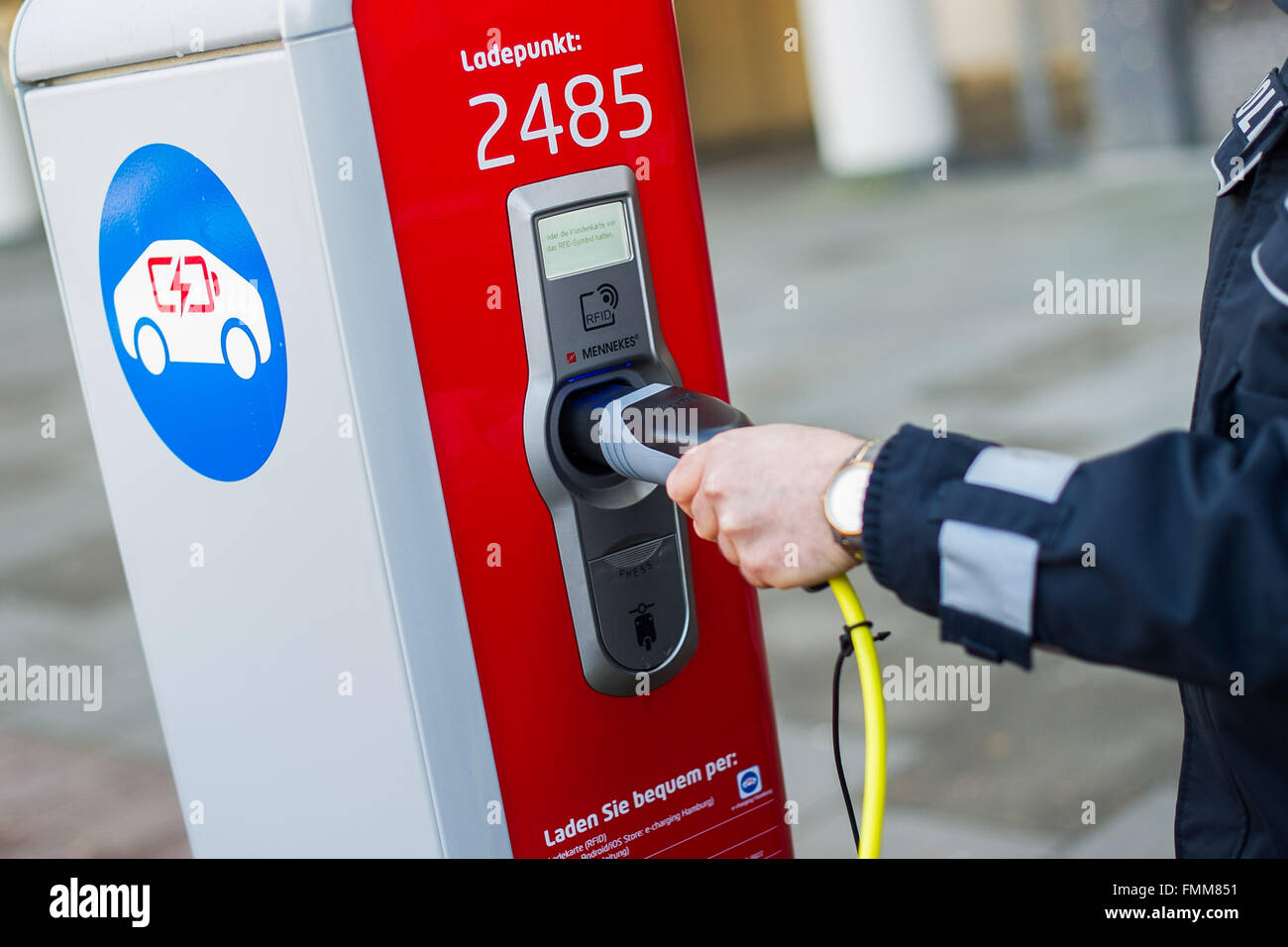 Hambourg, Allemagne. 09Th Mar, 2016. Un agent de police insère une fiche dans un pôle de charge pour les voitures électriques à Hambourg, Allemagne, 09 mars 2016. La ville de Hambourg a mis en place un nouveau mât de charge y compris de nouveaux signes d'un parking gratuit et de charge des voitures électriques sur Schoenhausener Allee (lit. Schoenhausen Avenue). Photo : Lukas SCHULZE/dpa/Alamy Live News Banque D'Images