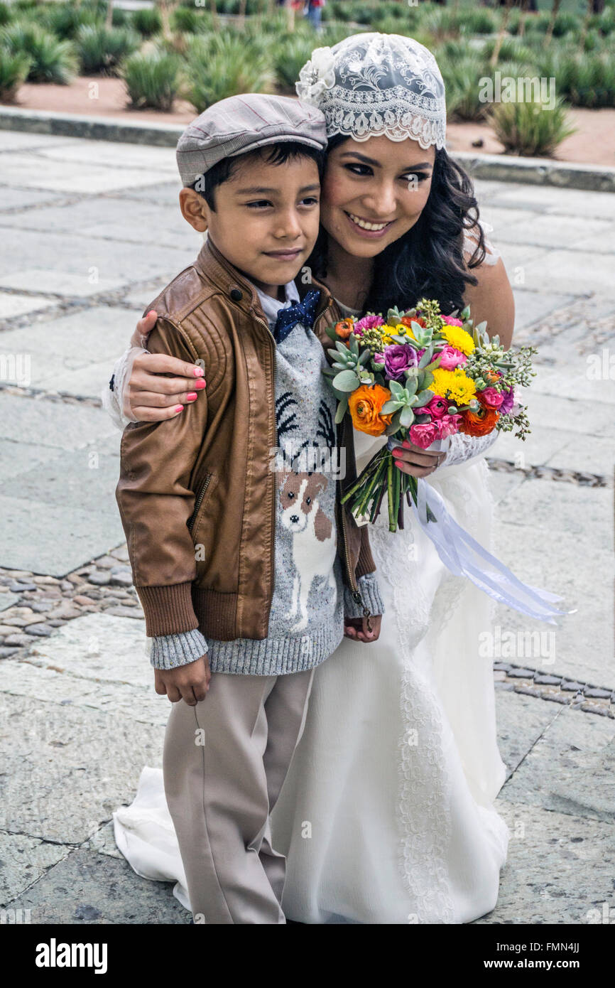 Heureuse mariée mexicain détient les fleurs du printemps et s'agenouille pour embrasser petit neveu pour photo de mariage à l'église de Santo Domingo Plaza Banque D'Images