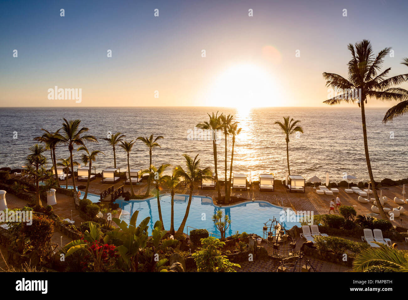 Une piscine au bord de mer avec des palmiers au coucher du soleil, Costa Adeje, Tenerife, Canaries, Espagne Banque D'Images