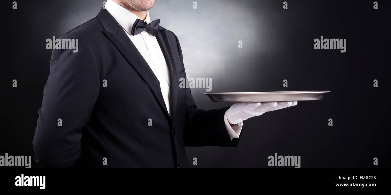 Waiter holding empty silver tray sur fond noir Banque D'Images