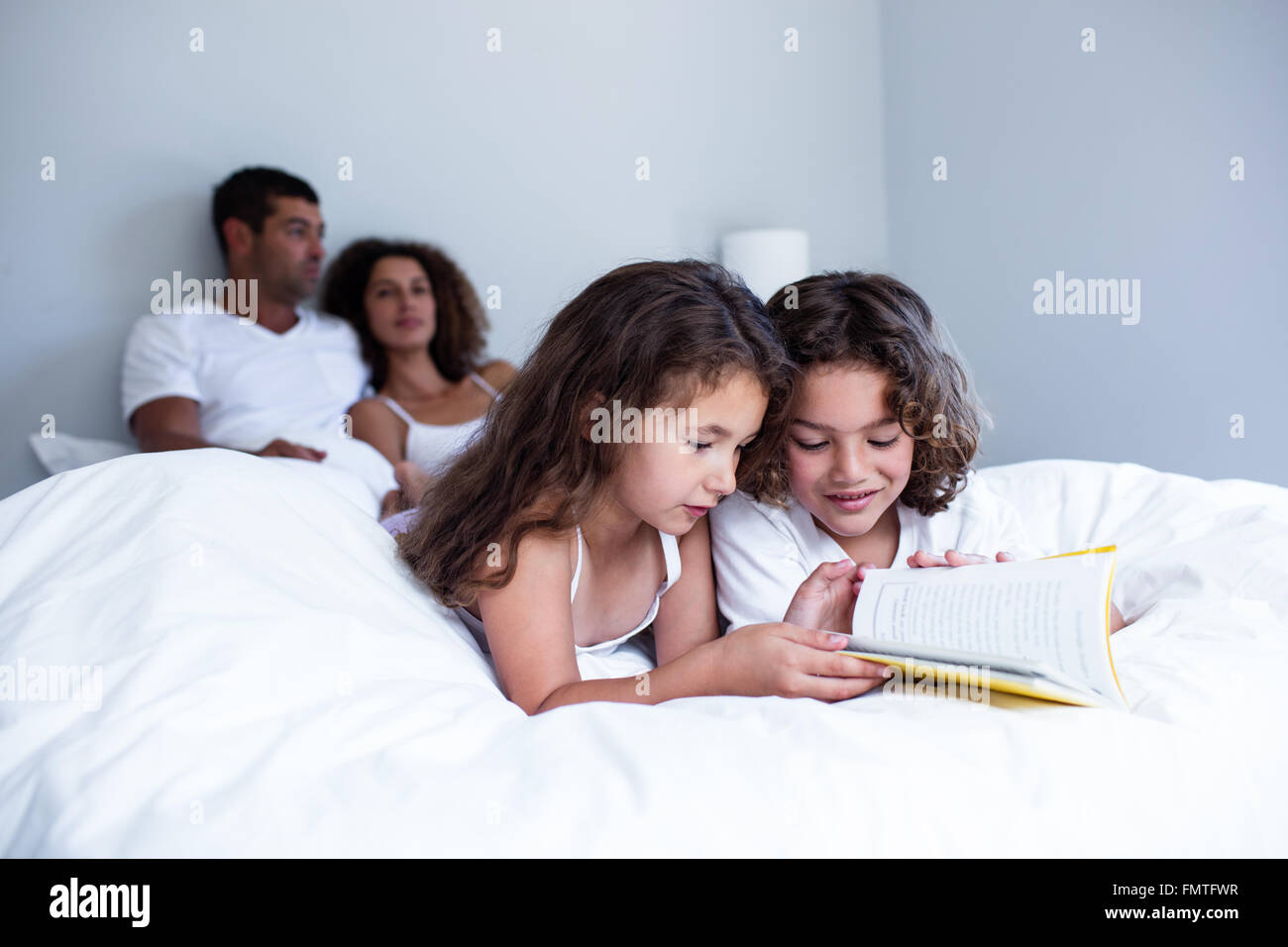 Frère et sœur reading book together on bed Banque D'Images