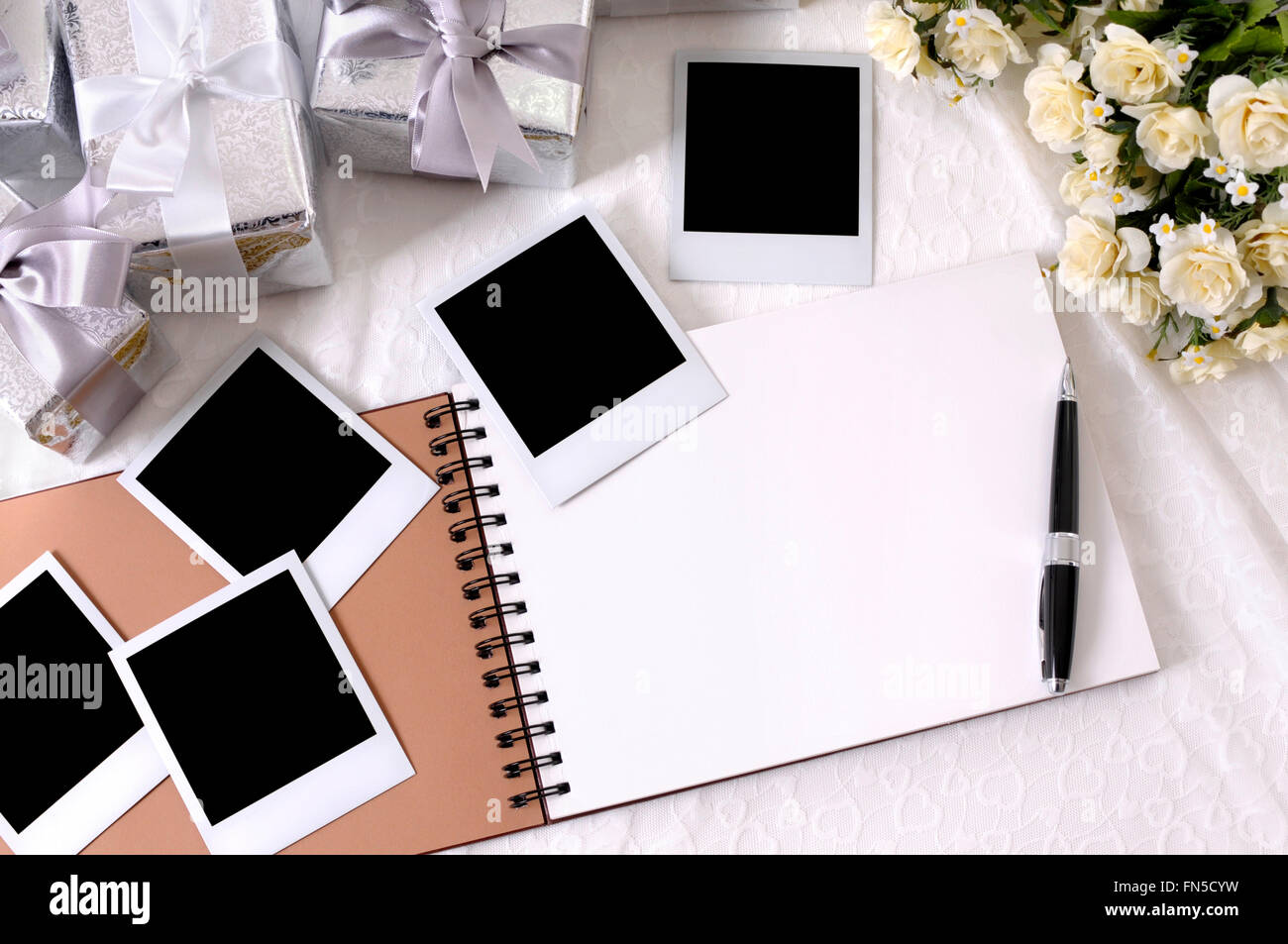 Album photo avec impressions photo instantanée vide posé sur la dentelle mariée avec plusieurs cadeaux de mariage d'argent et de roses blanches. Banque D'Images Album photo avec impressions photo instantanée vide posé sur la dentelle mariée avec plusieurs cadeaux de mariage d'argent et de roses blanches. Banque D'Images