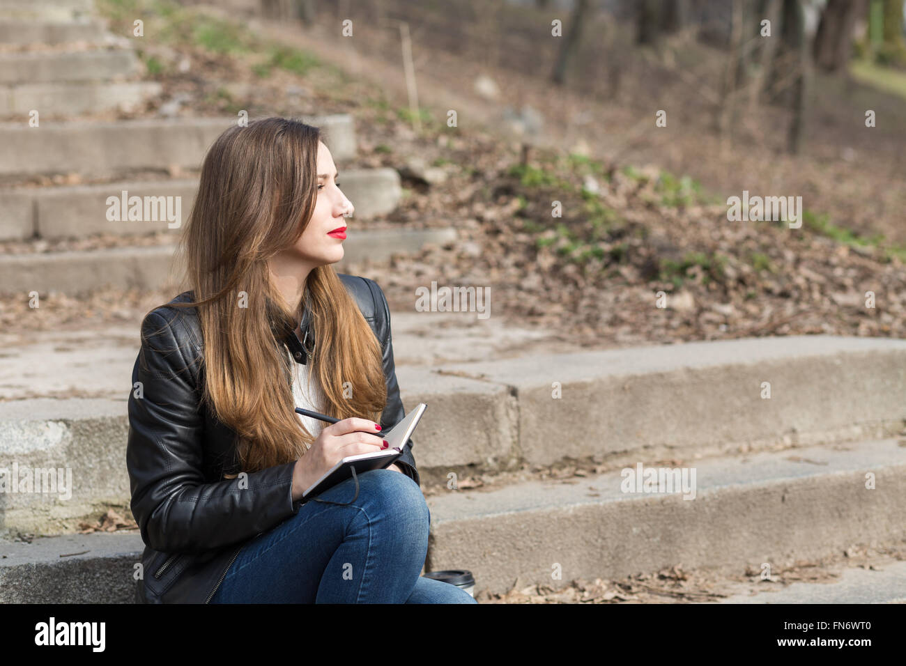 Jeune femme assise sur les marches dans le parc des dessins d'un pad. Thoughtful woman avec ordinateur portable sur des marches en pierre Banque D'Images