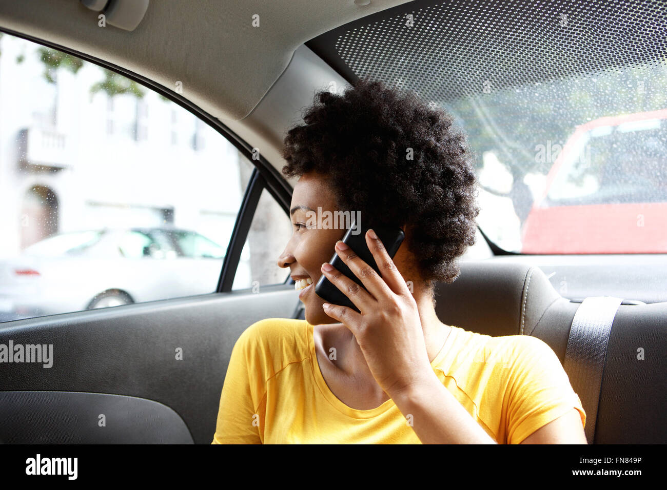 Close up portrait of young African woman sitting in siège arrière d'une voiture avec un téléphone mobile Banque D'Images