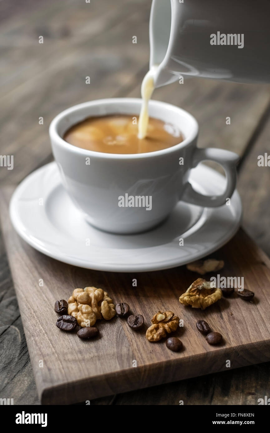 On verse la crème dans un café dans une tasse blanche. Banque D'Images