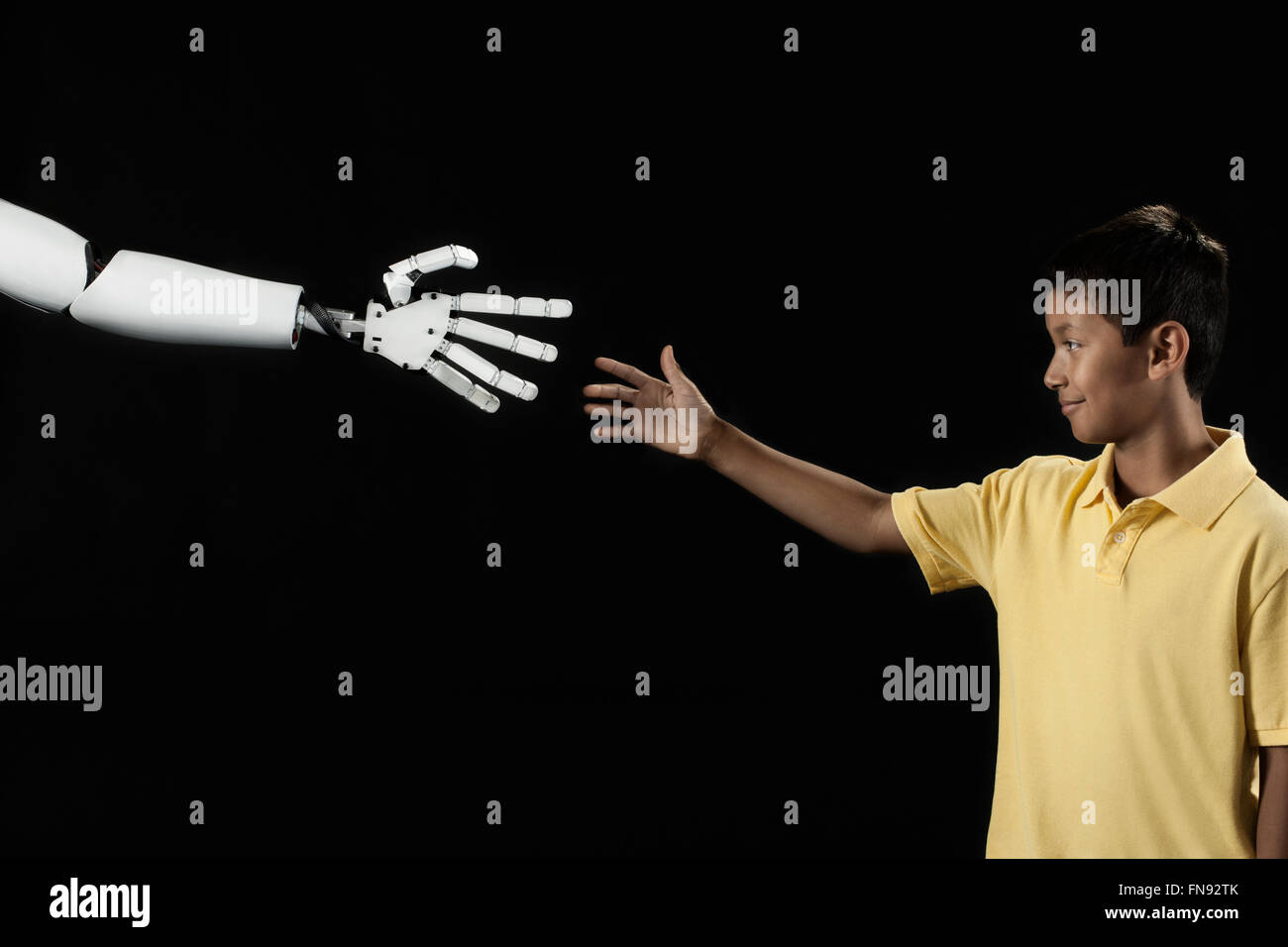 Un garçon atteignant jusqu'à toucher une main robotique. Banque D'Images