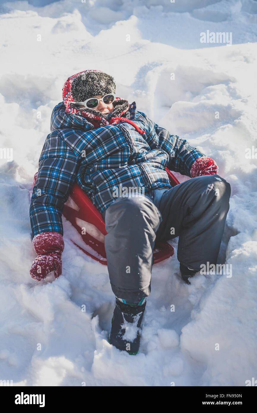 Garçon assis sur un traîneau dans la neige Banque D'Images