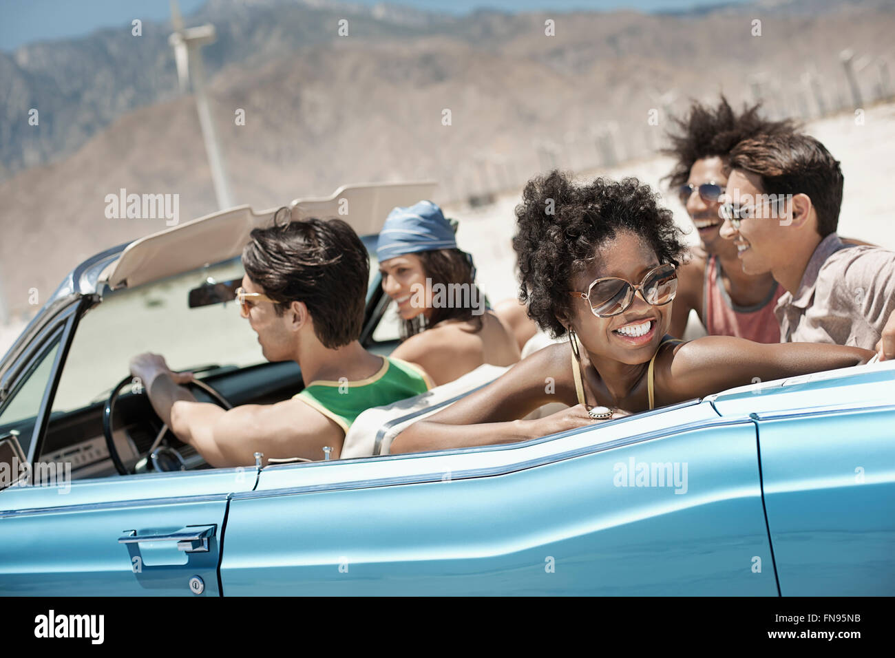 Un groupe d'amis dans un cabriolet bleu pâle sur la route, la conduite à travers une plaine entourée de montagnes. Banque D'Images