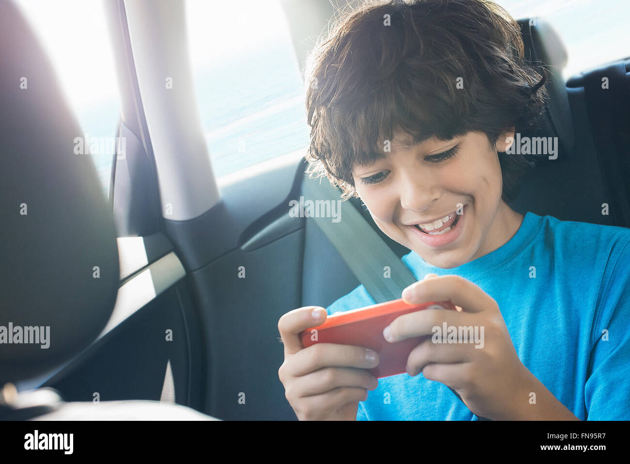 Un garçon assis dans une voiture à l'aide d'une tablette de jeux de poche. Banque D'Images