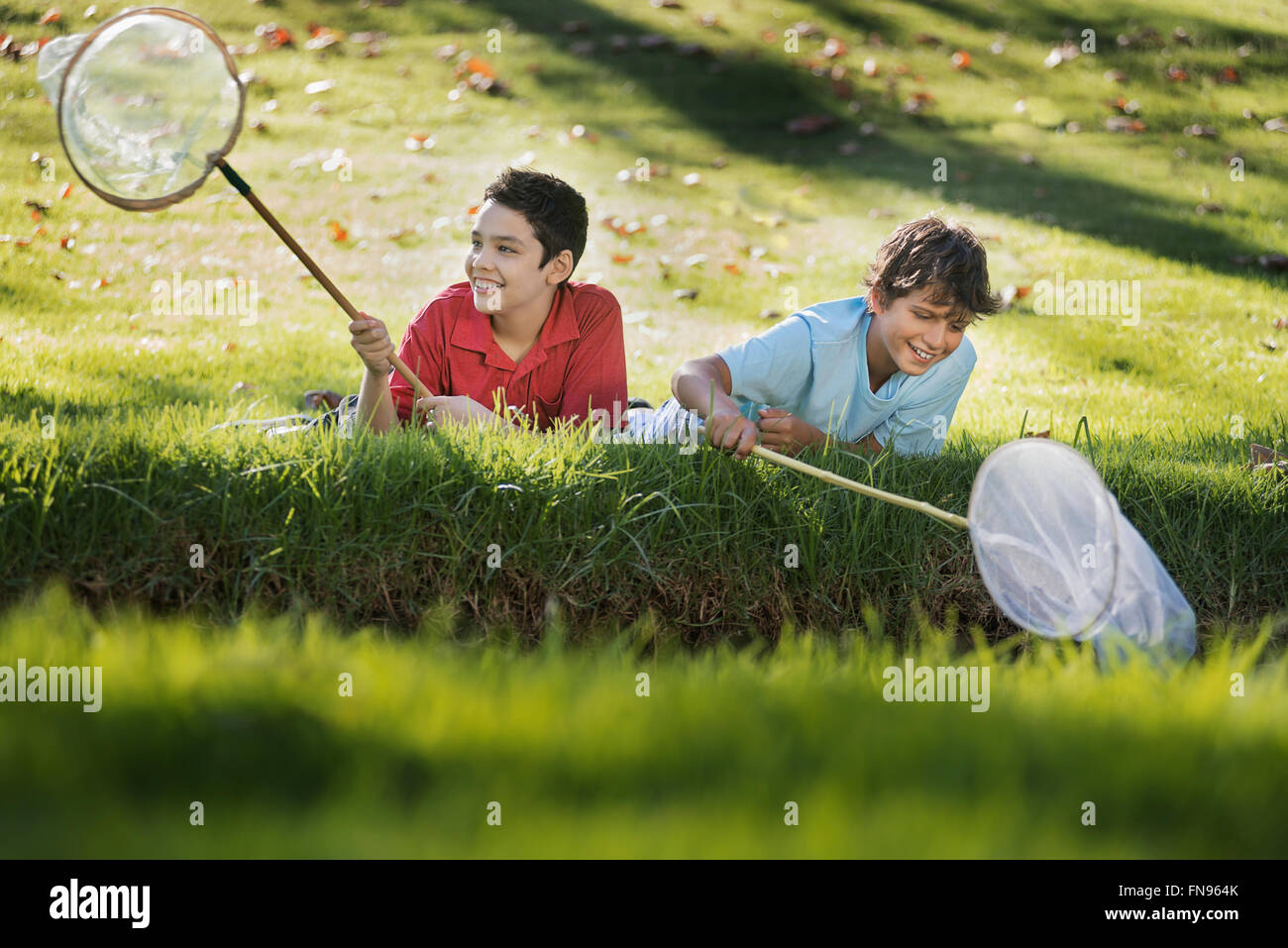 Deux garçons couchés sur l'herbe au bord d'un étang, à l'aide de filets de trempage de l'étang. Banque D'Images