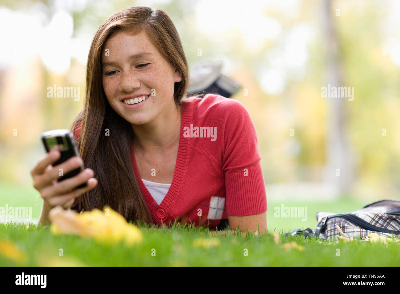 Une jeune fille couchée sur l'herbe à l'aide d'un téléphone mobile. Banque D'Images