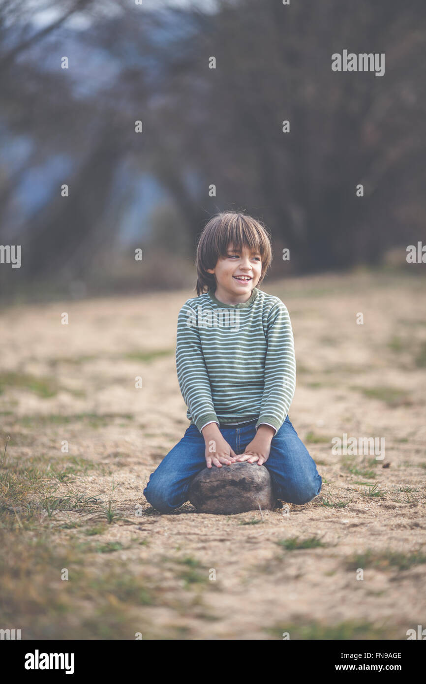 Smiling boy assis sur un rocher Banque D'Images