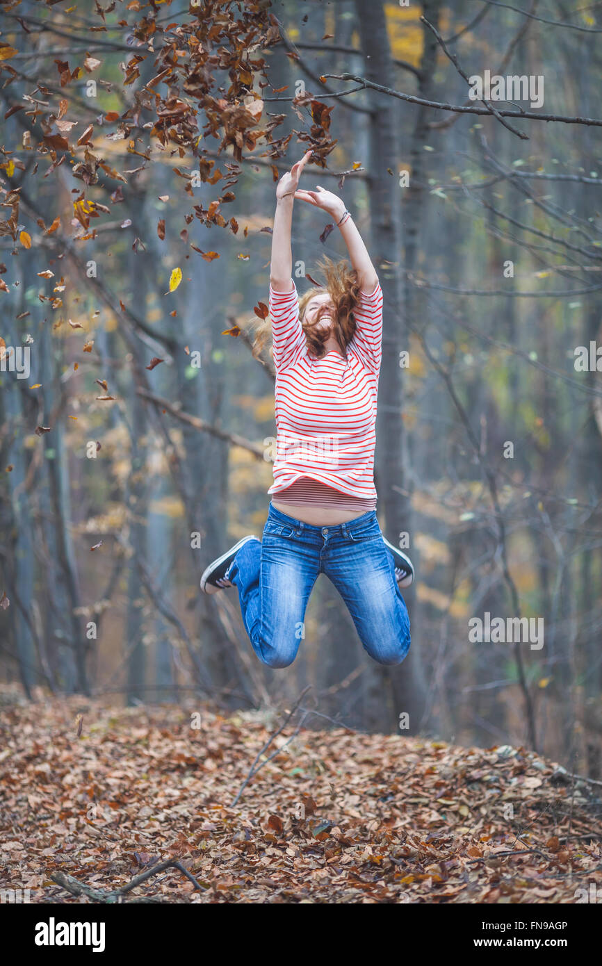 Mid adult woman sautant en l'air dans l'aménagement forestier Banque D'Images