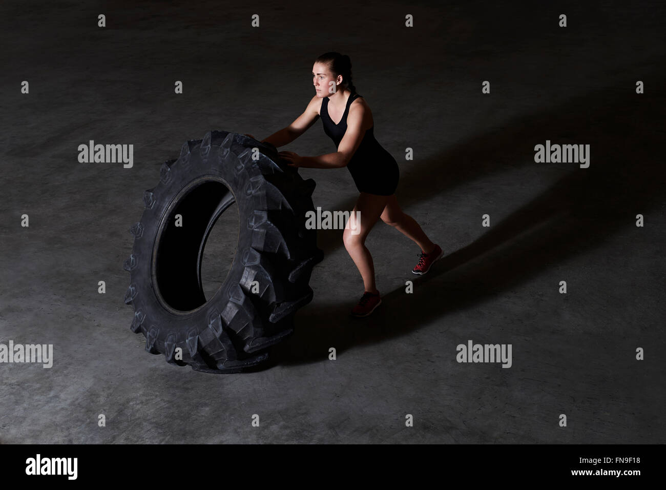 Femme poussant le pneu du tracteur en salle de sport Banque D'Images
