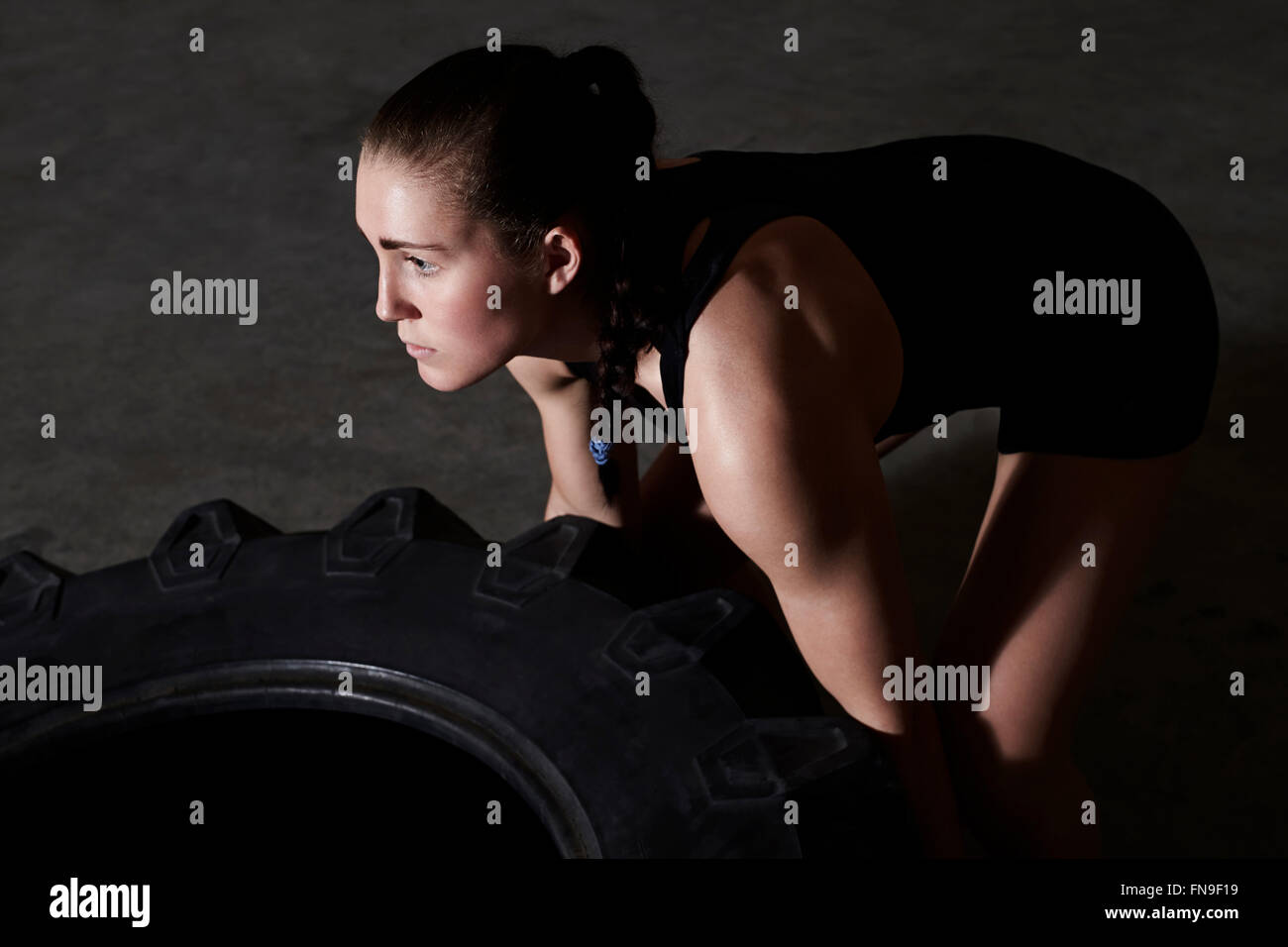 Woman lifting le pneu du tracteur en salle de sport Banque D'Images