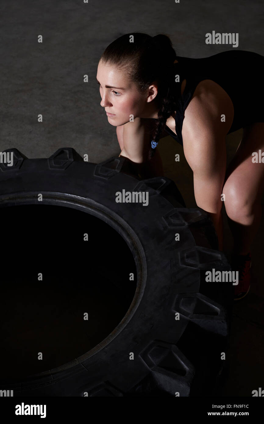 Woman lifting le pneu du tracteur en salle de sport Banque D'Images