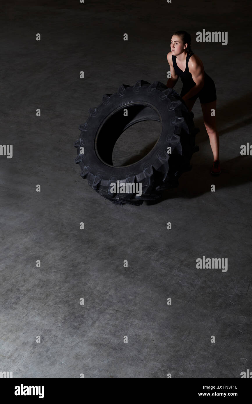 Woman lifting le pneu du tracteur en salle de sport Banque D'Images
