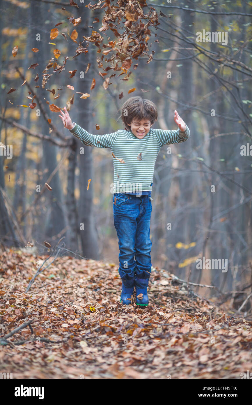 Garçon sautant et jeter les feuilles d'automne dans l'air Banque D'Images