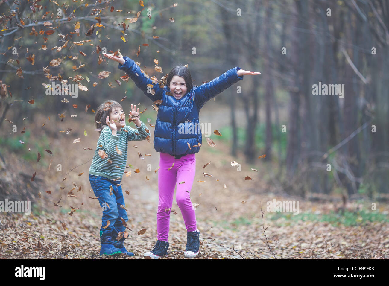 Garçon et fille de jeter les feuilles d'automne dans l'air Banque D'Images