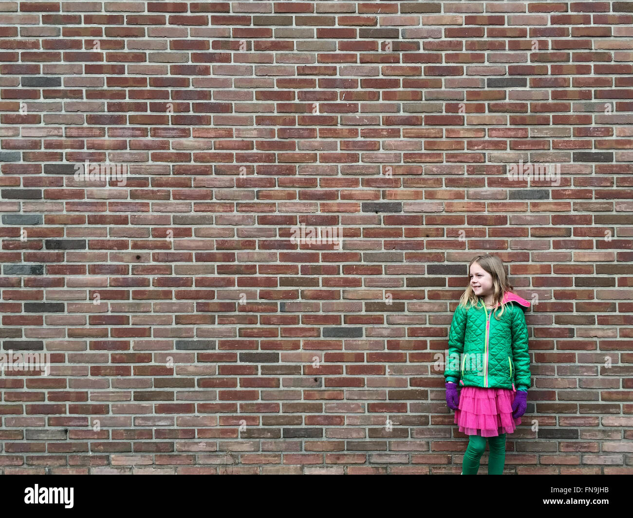 Smiling Girl standing in front of brick wall Banque D'Images