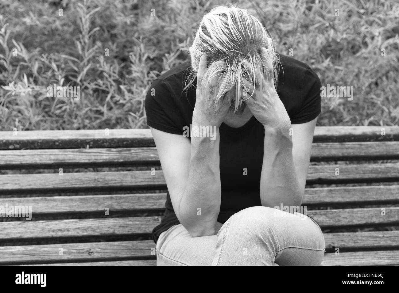 Monochrome avant portrait d'une femme d'âge moyen frustré assis sur un banc en bois à l'extérieur et appuie tête par les mains. Banque D'Images
