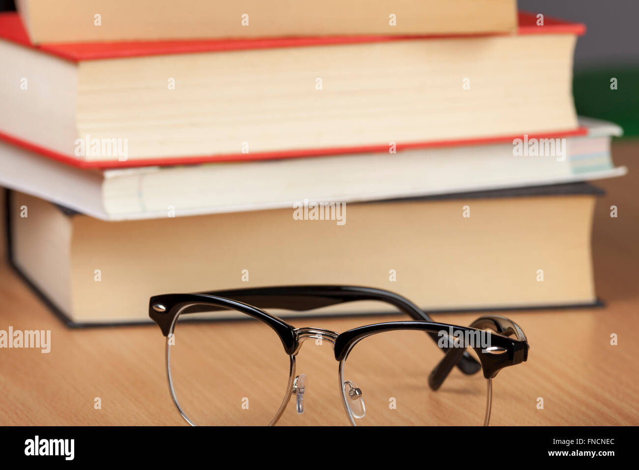 Paire de lunettes noir portant à côté d'une pile de livres à lire sur une table wodden Banque D'Images