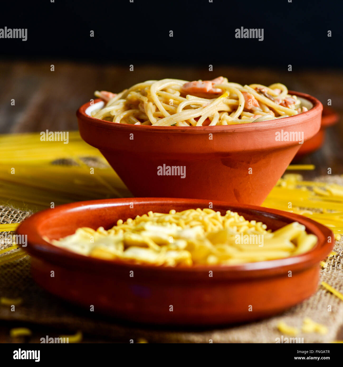 Libre d'une plaque en terre cuite avec quelques pâtes alimentaires non cuites et un bol de faïence avec spaghetti alla carbonara, sur une table Banque D'Images