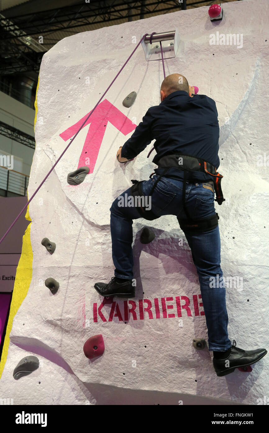 Homme sur un mur d'escalade au stand de Deutsche Telekom au CeBIT Digital Technology Trade Fair 2016 à Hanovre, Allemagne.Le mot « carrière » (ou « échelle de réussite ») est écrit sur le mur. Banque D'Images