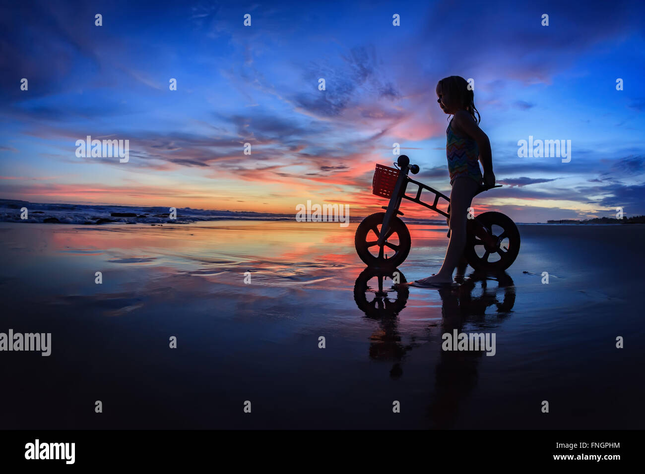 Silhouette noire du petit enfant - run bike rider debout sur le sable humide, regardez en mer et surf sunset sky coloré. Banque D'Images