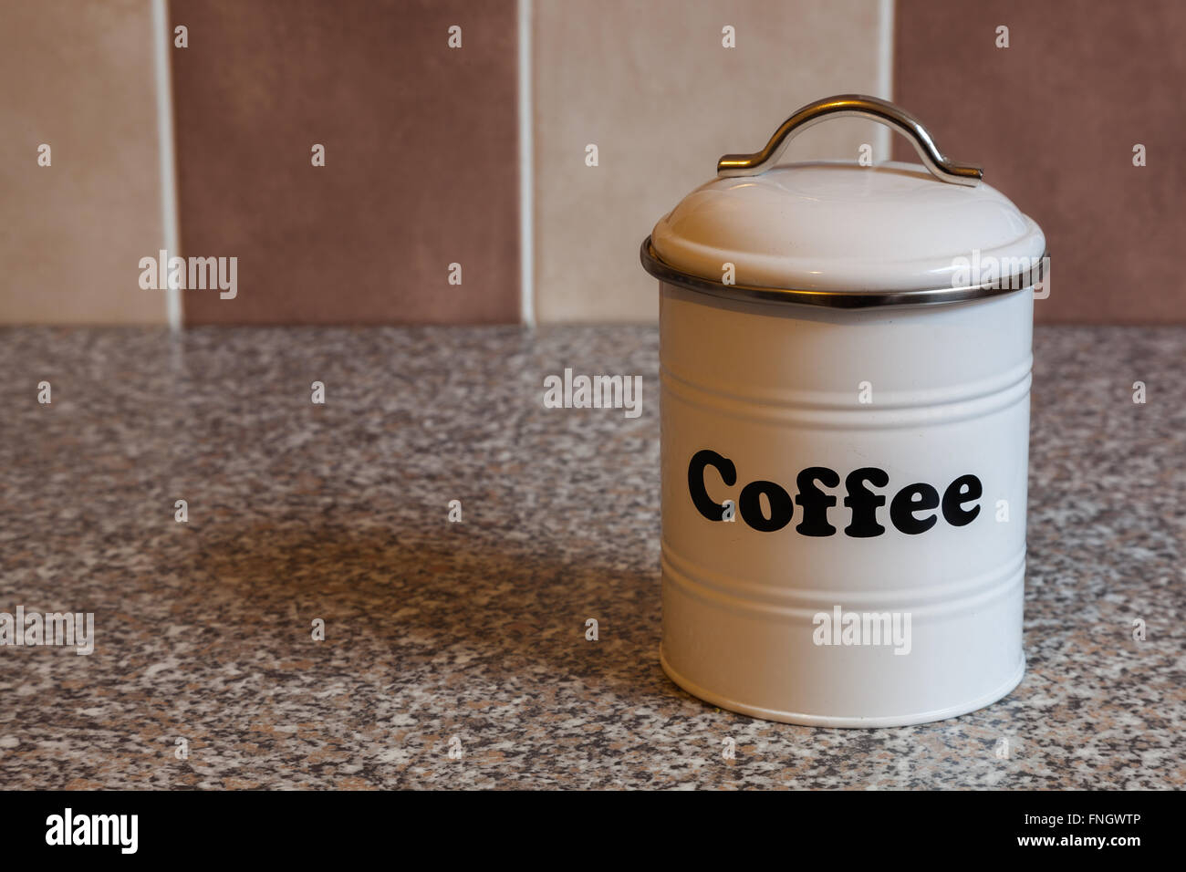 Cartouche blanc pour le stockage du café sur un plan de travail de cuisine en granit avec carreaux marron et beige. Banque D'Images