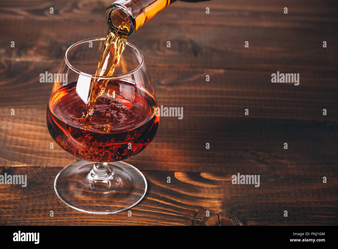 Verser le brandy ou cognac de la bouteille dans le verre contre le fond de bois Banque D'Images