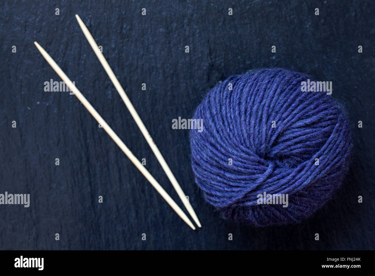 Pelote de fil violet avec des aiguilles à tricoter en bambou avec fond en ardoise noire Banque D'Images