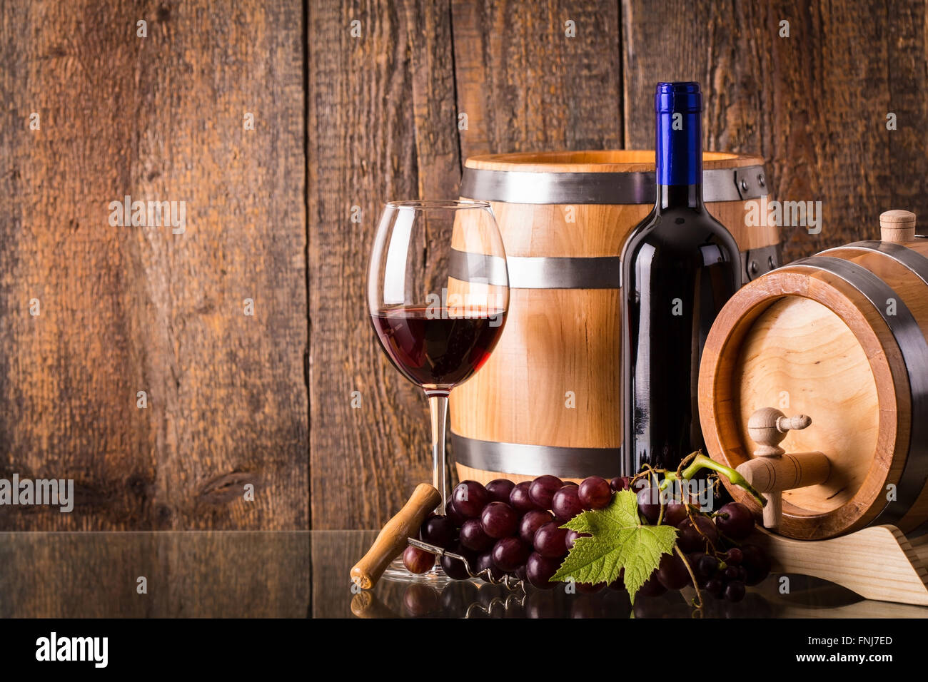 Verre de vin rouge avec bouteille sombre baril raisins et fond de bois Banque D'Images