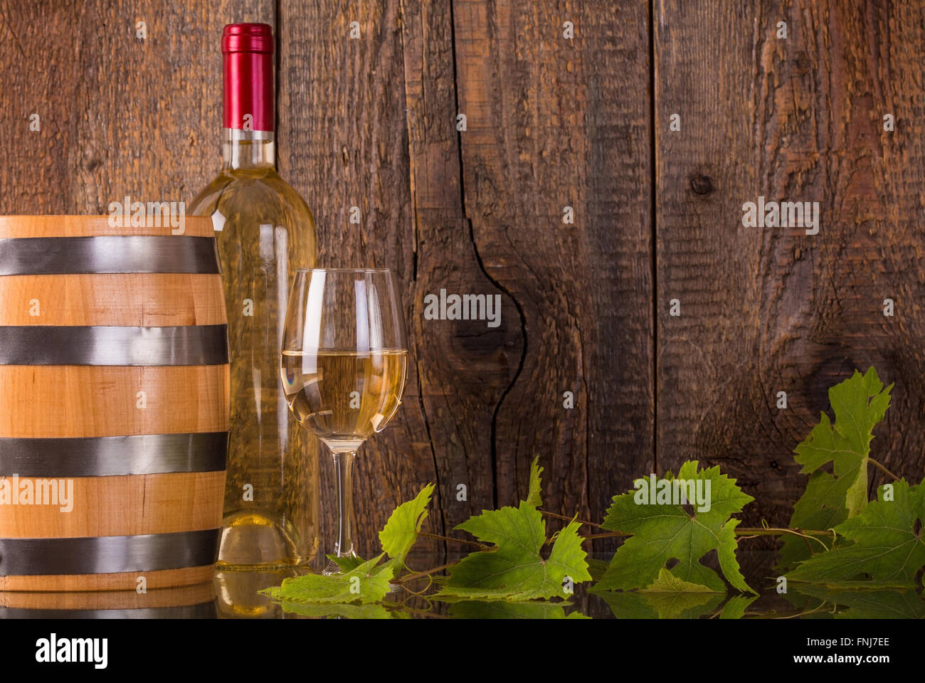 Verre de vin en bouteille blanche baril grapeleaves et fond en bois foncé Banque D'Images