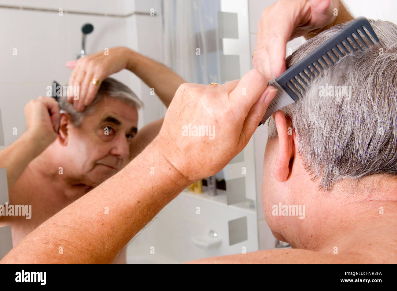 Un homme âgé se peigner ses cheveux et à la recherche en miroir Photo Stock  - Alamy