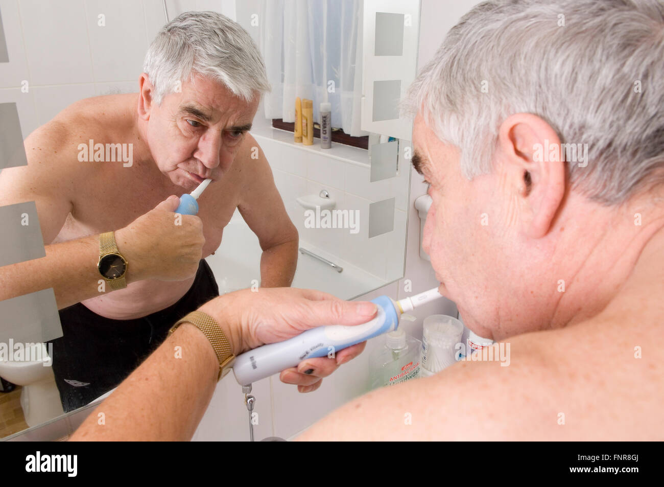 Un homme âgé se brosser les dents à l'aide d'une brosse à dents électrique. Banque D'Images