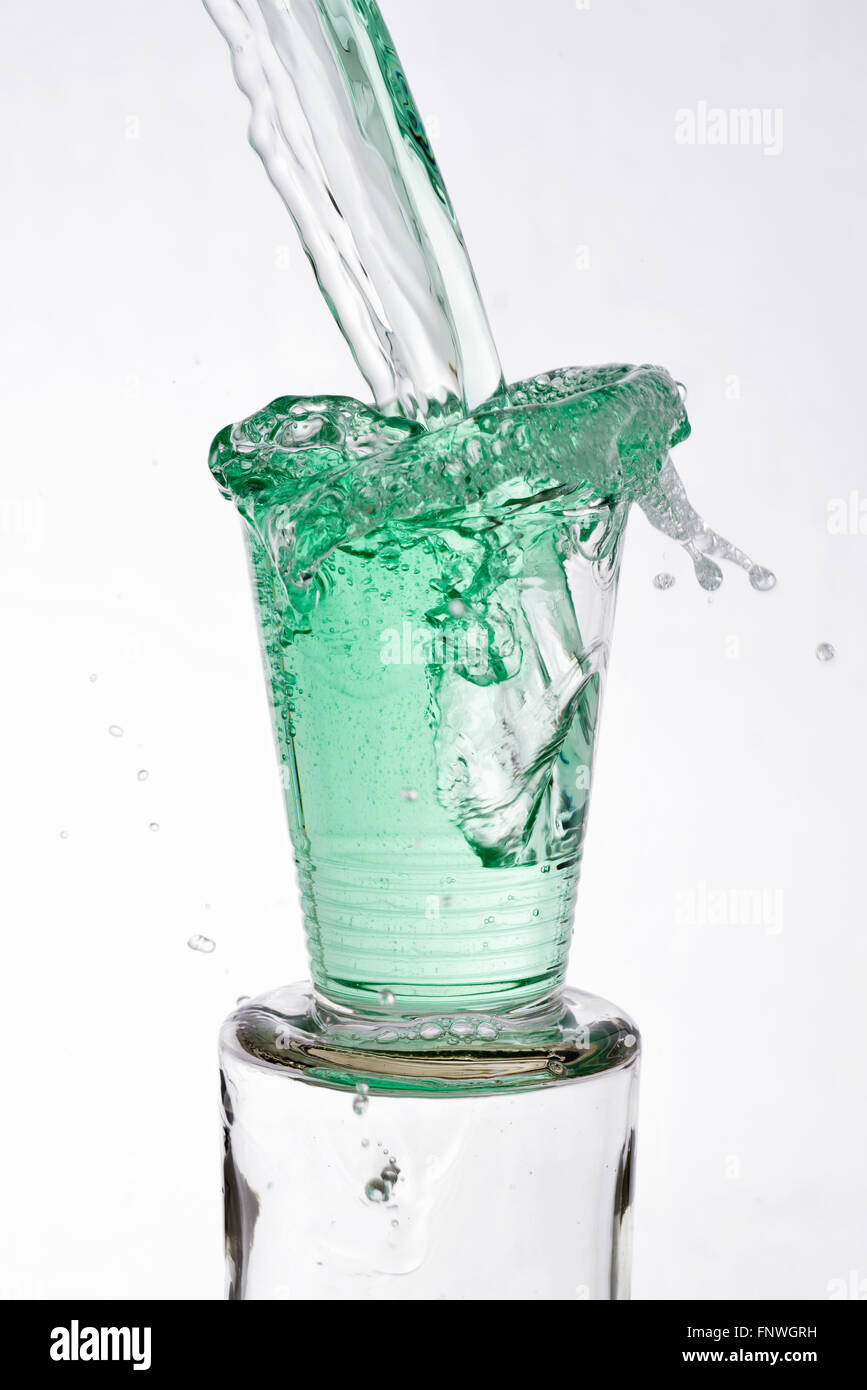Green drinks vigoureusement coulé éclaboussures débordante d'un verre, sur un fond blanc Banque D'Images