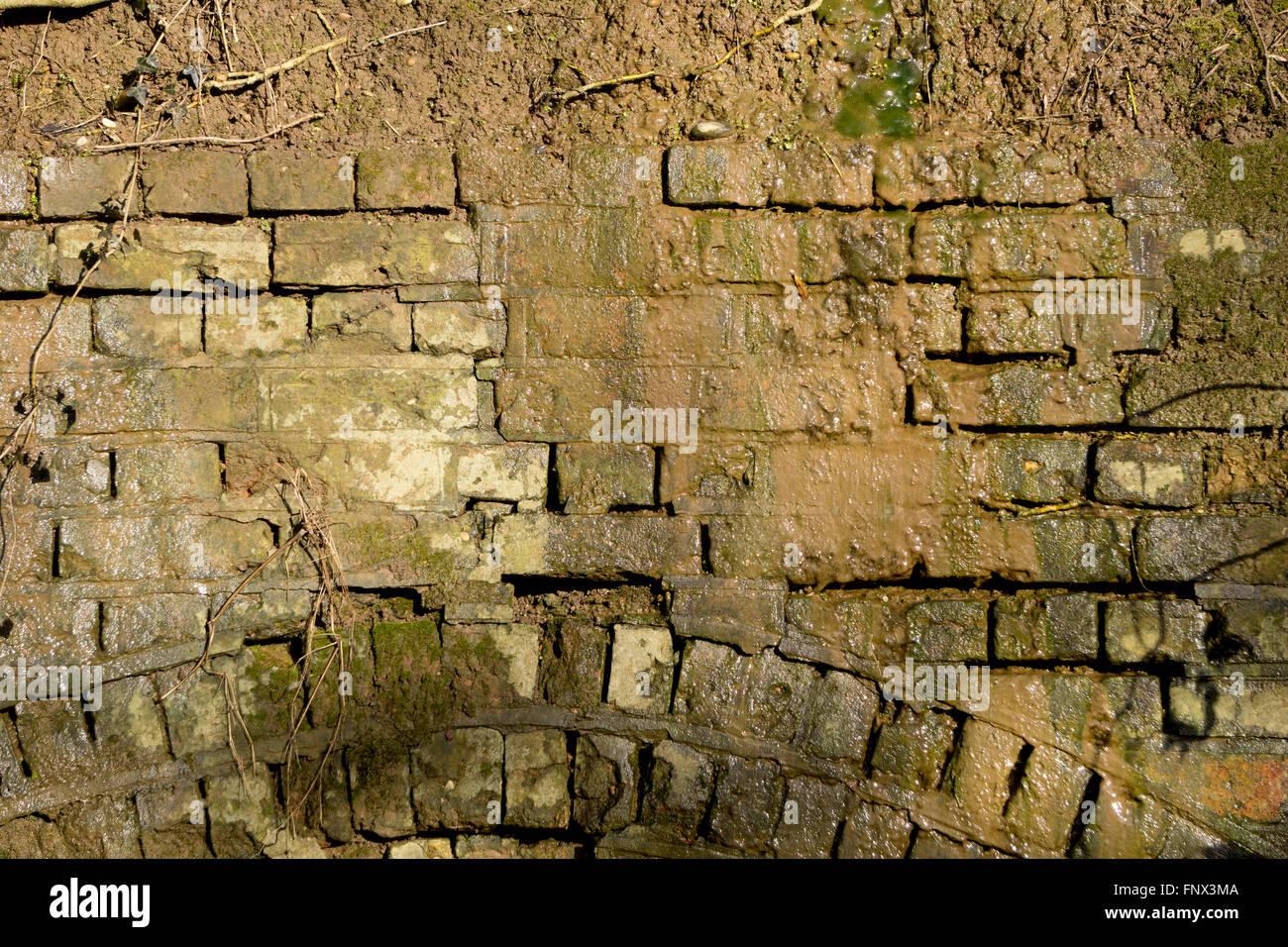 Mur de briques en ruine avec de l'eau fonctionnant en bas. Banque D'Images
