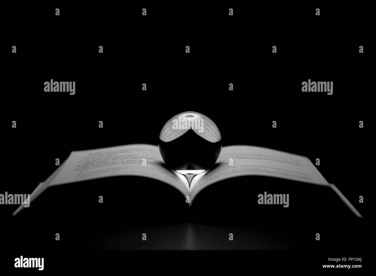 Livre ouvert et bille de verre sur un fond noir. Image clé faible. Banque D'Images