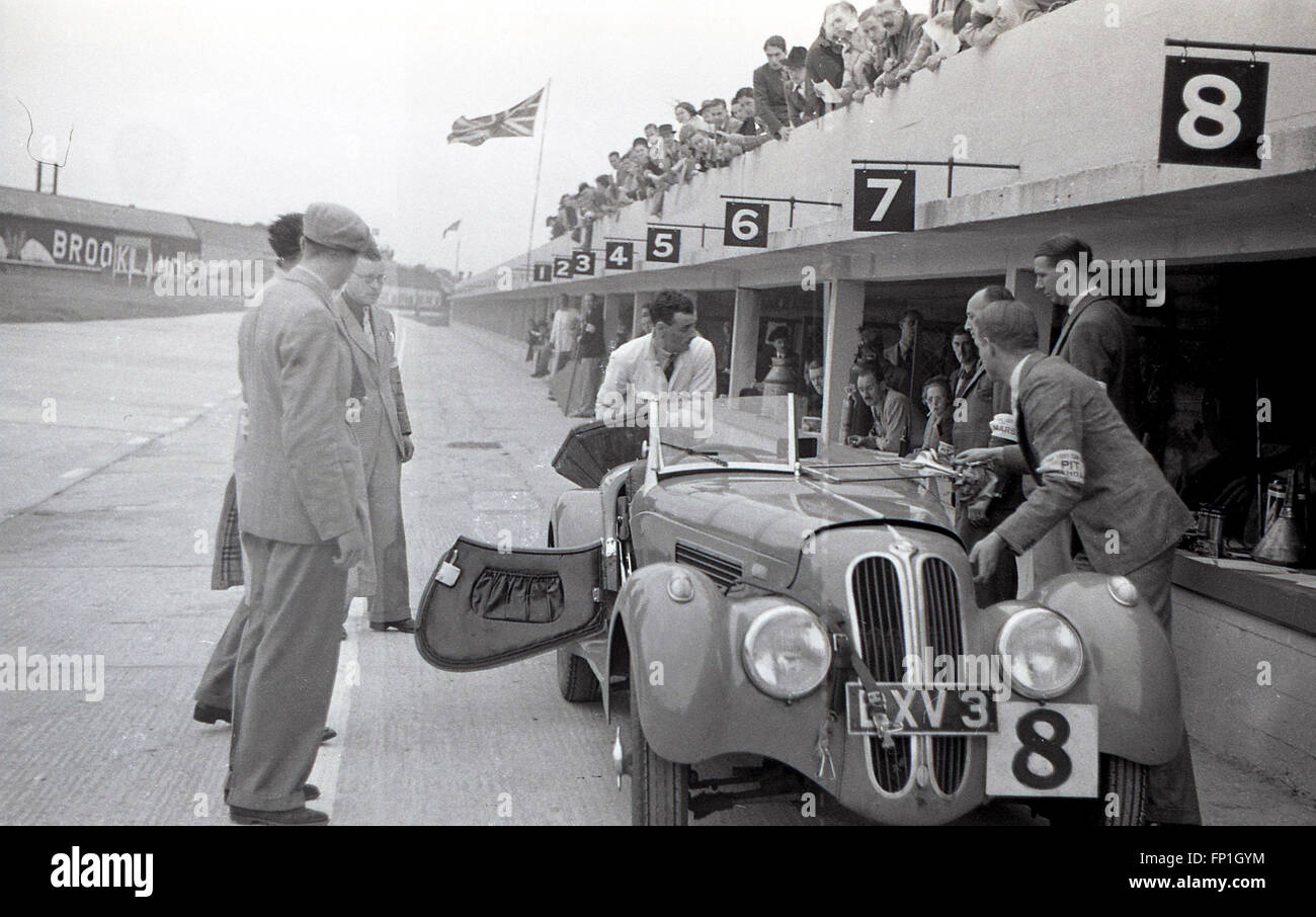 Années 1930, photo historique de la voie des stands du circuit de Brooklands, le premier circuit de course automobile au monde construit à cet effet, Weybridge, Surrey, Angleterre. Une voiture de course monoplace à toit ouvert, no 8, garée dans une voie sur le côté de la piste avec des spectateurs assis au-dessus du sol regardant. Banque D'Images