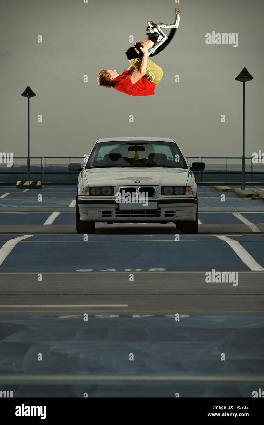 Jeune mec sur un jumping boots sautant par-dessus une voiture Banque D'Images