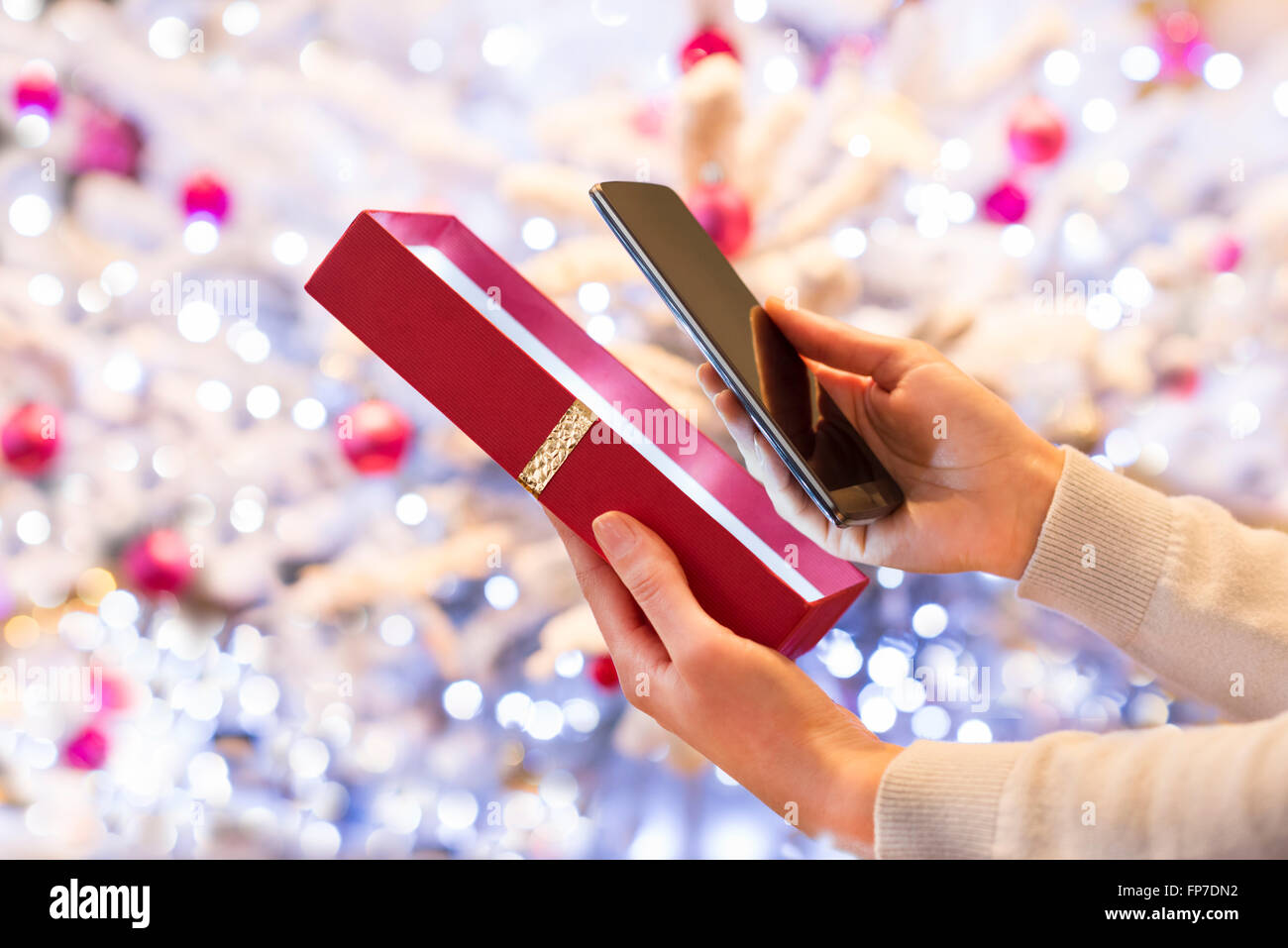 Femme découvre un smartphone en cadeau de Noël. Arrière-plan de l'arbre de Noël Boke Banque D'Images