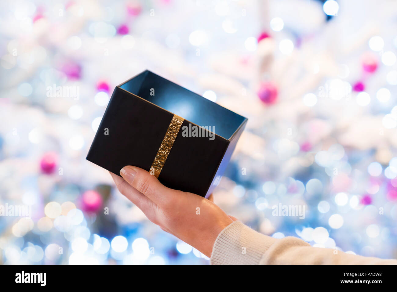Femme ouvre une boîte noire cadeau en face d'un arbre de Noël Banque D'Images