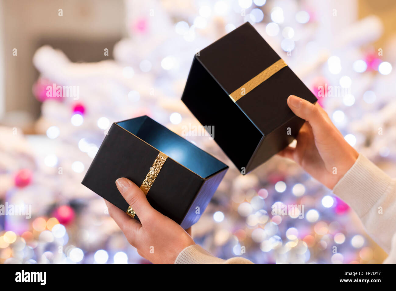 Femme ouvre une boîte noire présente en face d'un arbre de Noël Banque D'Images
