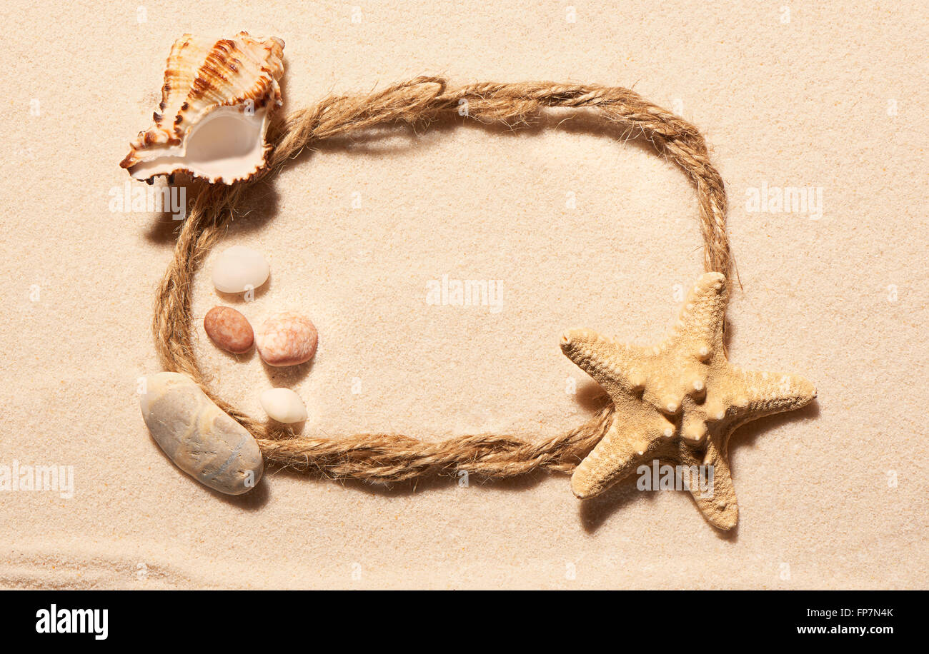 Cadre ovale de corde avec des étoiles de mer, coquillages de mer vide et des pierres sur le sable. Fond de plage d'été. Vue de dessus Banque D'Images