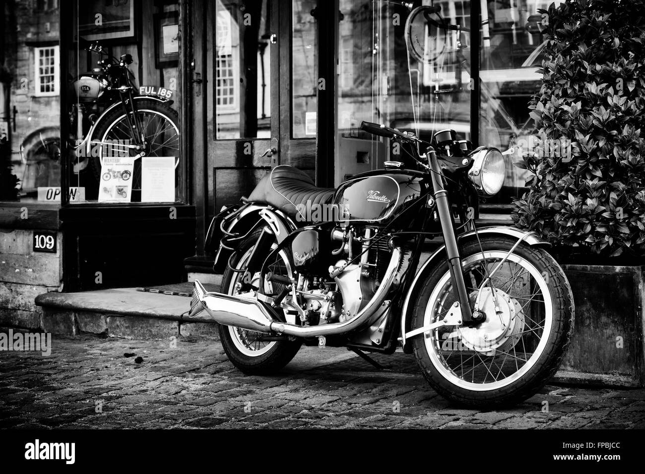 Moto Velocette Venom Clubman à l'extérieur d'un magasin d'antiquités à Burford, Oxfordshire, Cotswolds, en Angleterre. Le noir et blanc Banque D'Images
