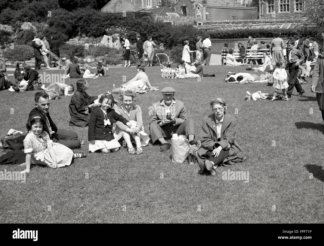 Historique années 1950, family sitting on grass à l'extérieur de maison historique. Banque D'Images