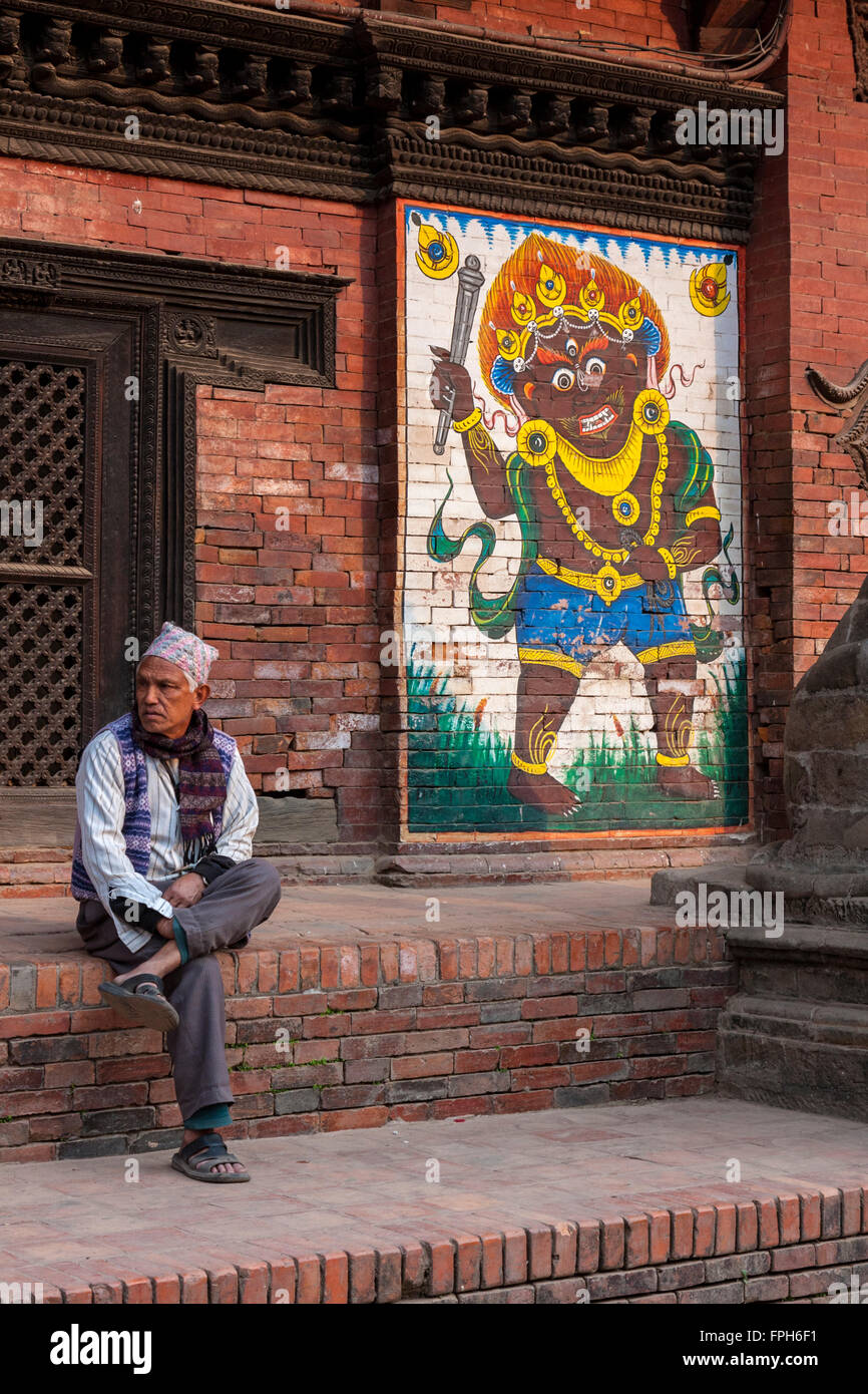 Le Népal, Patan, Durbar Square. L'homme assis à côté d'une peinture de Bhairab (Bhairav), une violente manifestation du Seigneur Shiva. Banque D'Images