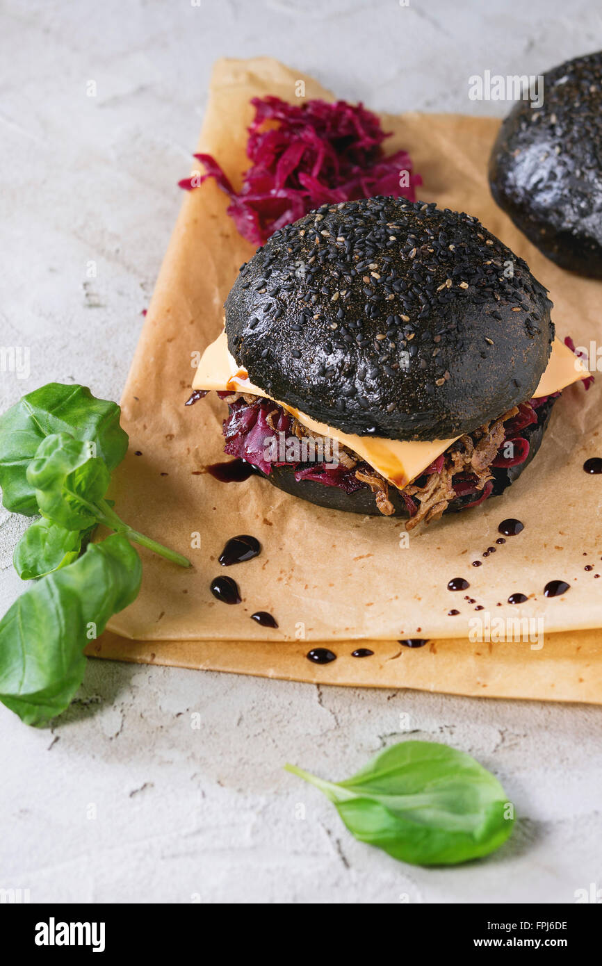 Burger de boeuf noir avec les ragoûts, fromage, choux rouge et sauce balsamique servi sur du papier sulfurisé avec le basilic sur plâtre gris Banque D'Images